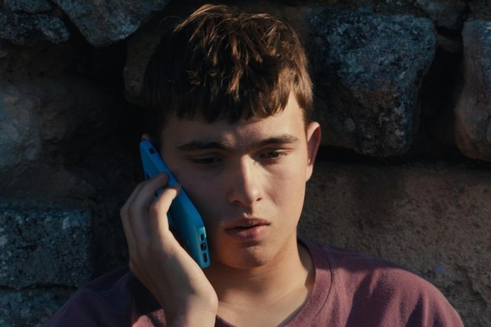 Enzo still: a young man leaning against a rock on the phone.