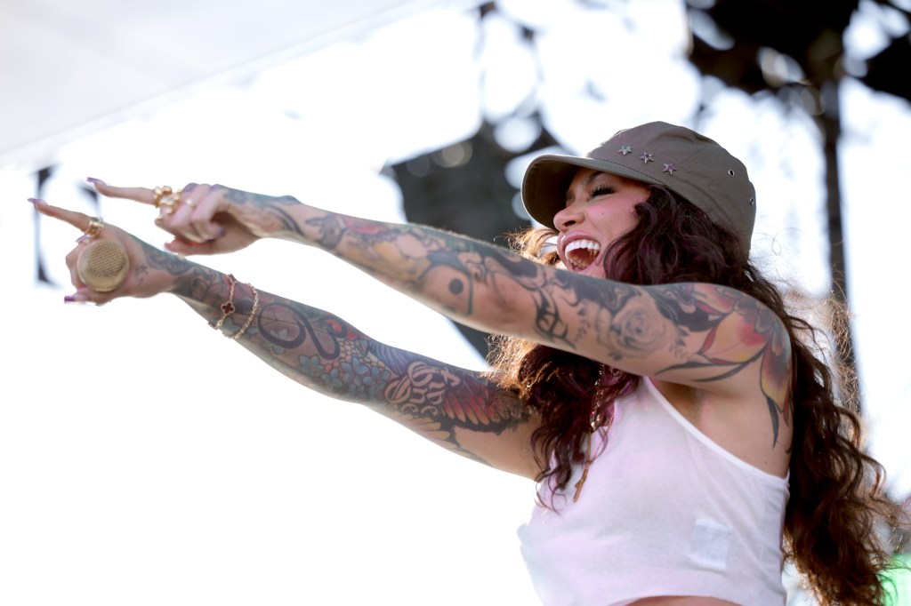 Kehlani performs onstage. Her amrs are outstreched, pointing to the audiecne while smiling.
