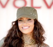 Kehlani smiling at the camera with a green hat and gold hoops and necklaces.