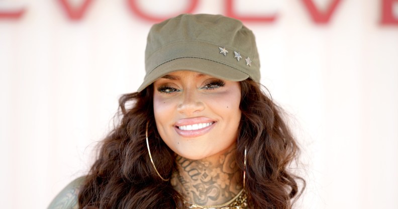 Kehlani smiling at the camera with a green hat and gold hoops and necklaces.