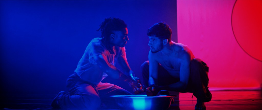 Night Stage still: two men crouched over a bowl, blue and pink light behind them