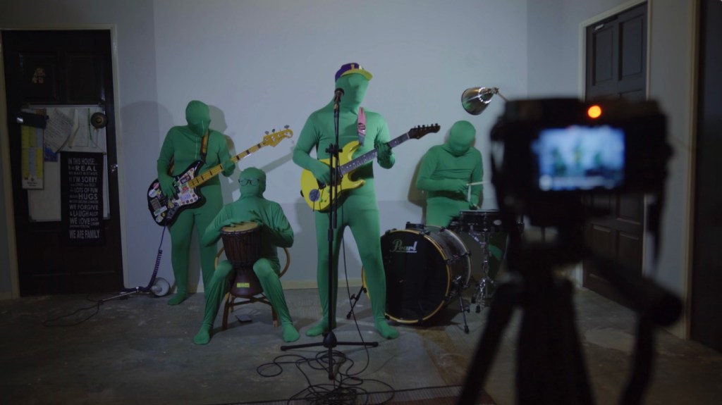 Queer As Punk still: a band in green screen suits