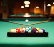 Plastic triangle rack with billiard balls and cues on green table indoors