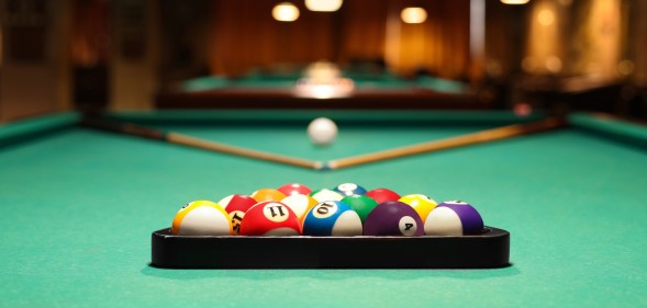 Plastic triangle rack with billiard balls and cues on green table indoors