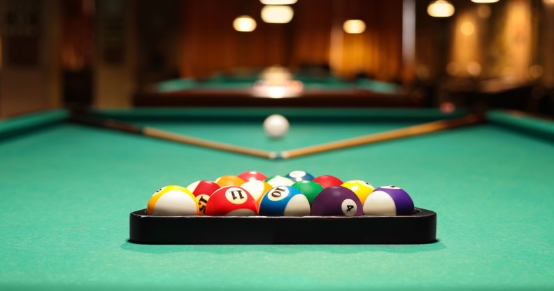 Plastic triangle rack with billiard balls and cues on green table indoors