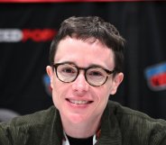 Elliot Page attends New York Comic Con. Eliott wearing a green cordoroy jacket smiling into the camera, wearing round glasses.