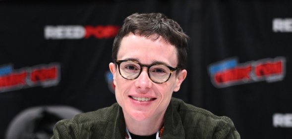 Elliot Page attends New York Comic Con. Eliott wearing a green cordoroy jacket smiling into the camera, wearing round glasses.