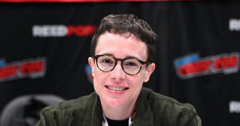 Elliot Page attends New York Comic Con. Eliott wearing a green cordoroy jacket smiling into the camera, wearing round glasses.