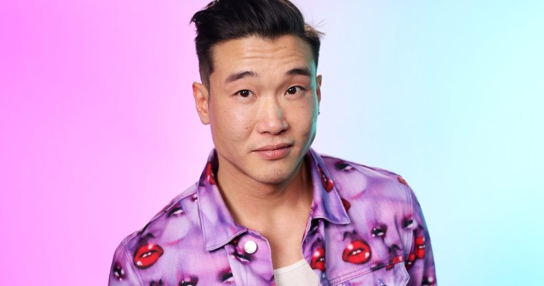 Joel Kim Booster in a jacket with purple faces and red lips. The background is hazy pink and blue.
