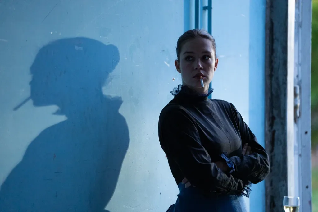 Another Day still: a woman smoking, behind her on a blue wall her extended shadow