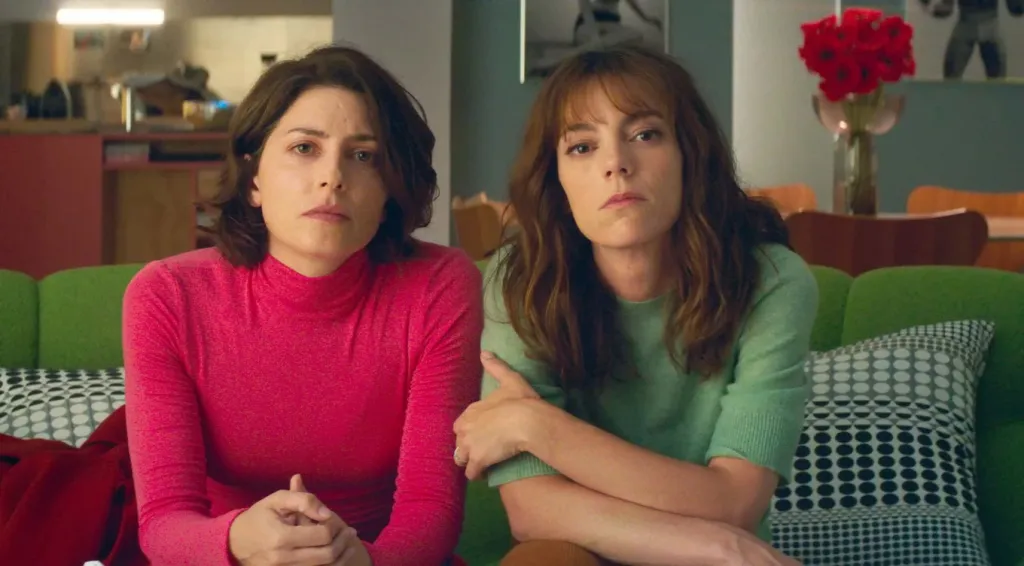 Bitter Christmas still: two women staring into the camera, sat close on a sofa