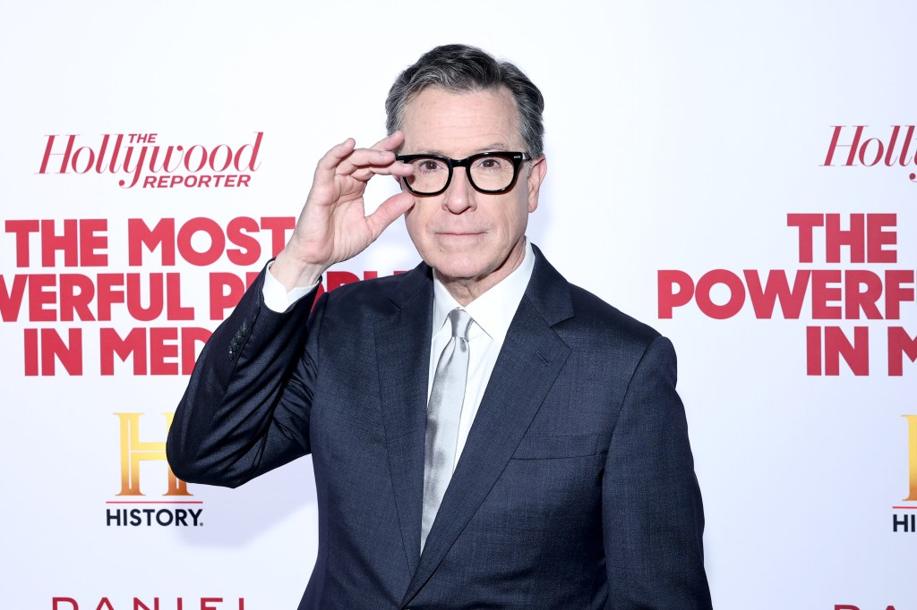 Stephen Colbert in a suit, holding his glasses