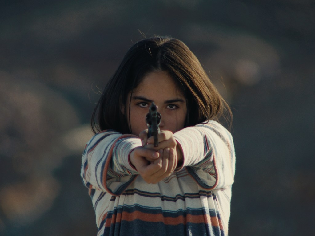 The Mysterious Gaze of the Flamingo: a young girl pointing a gun at the camera.