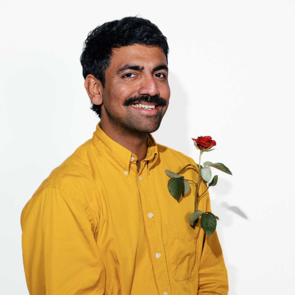 Adi Parmar wearing a yellow shirt and holding a red rose.