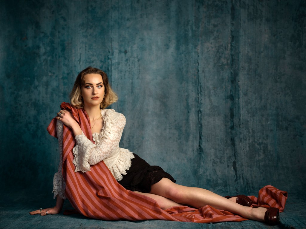 Amy Matthews: Definitions of Toast. Amy lying on a pink stipped blanket against a blue-grey background.