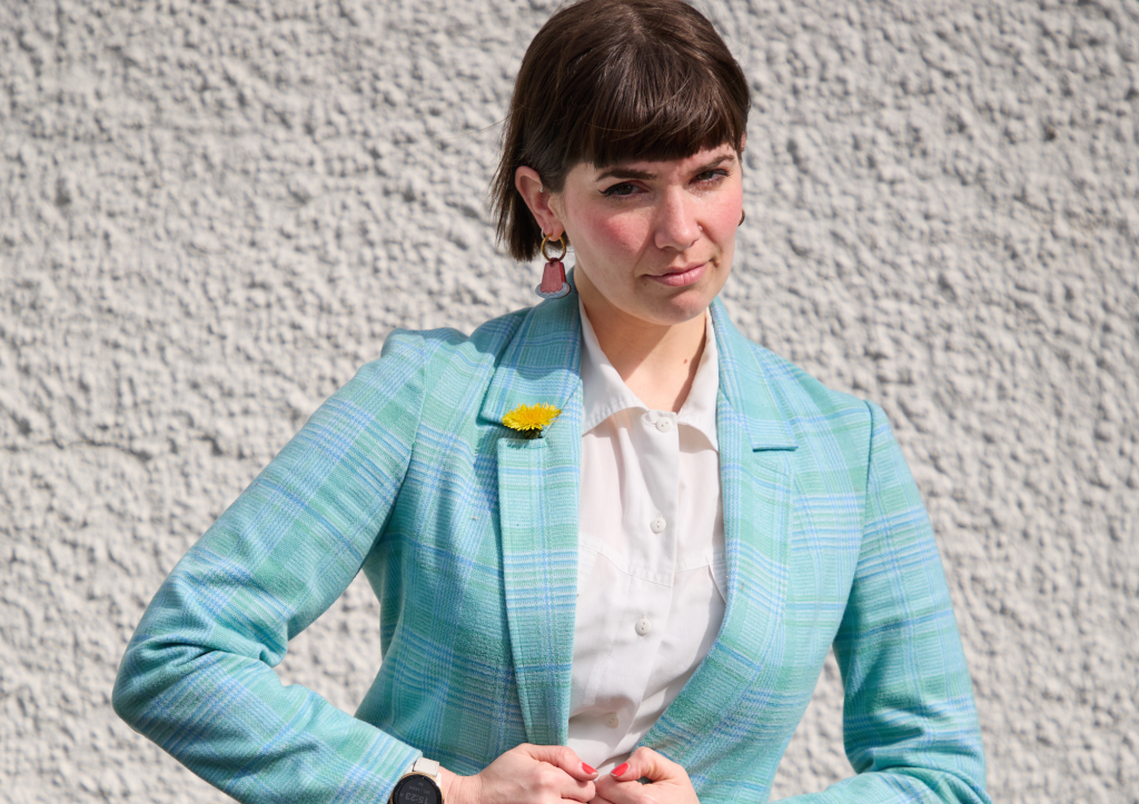 Kate Hammer: Government Approved Comedian. Kate buttoning a blue suit.