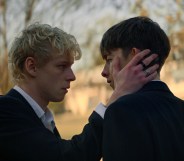 Leviticus still: two teen boys, the blonde cradling the cheek of the brunet, both in suits.