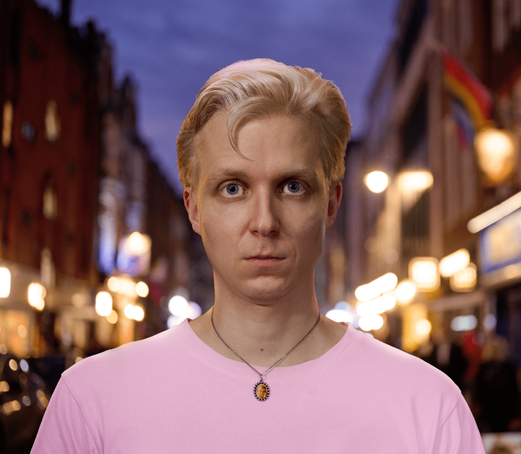 Linus Karp Was Hit With an Umbrella: a man in a pink t shirt on a street looking into the camera.