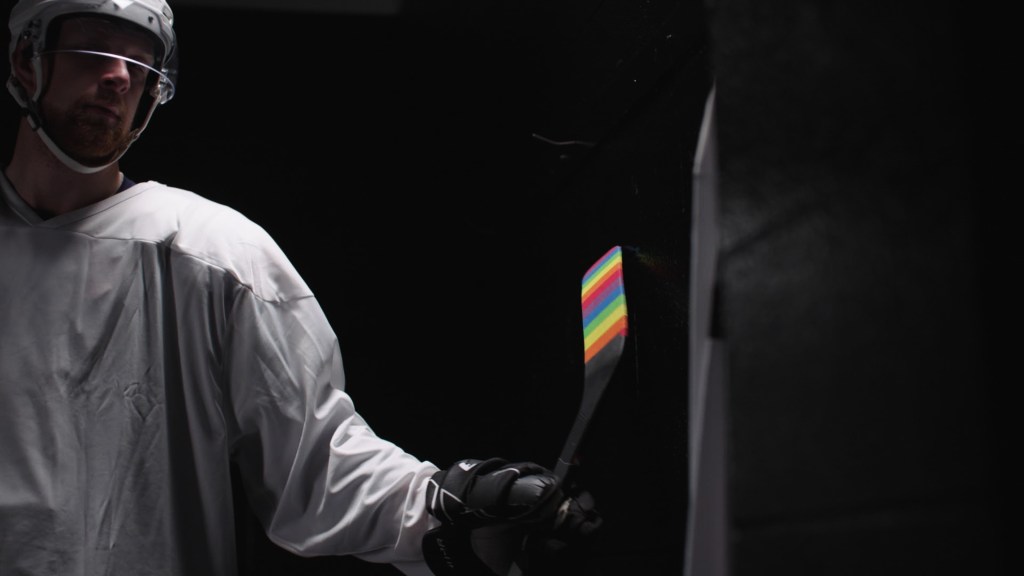 The Hockey Player still: Luke Prokop in ice hockey gear holding a stick with pride tape