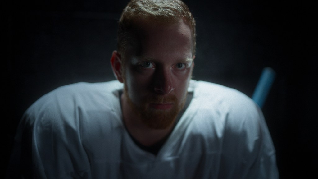 The Hockey Player still: Luke Prokop looking into the camera, wearing ice hockey gear in a dark rink