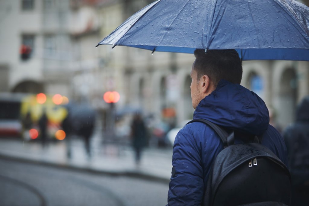 Man holding wet umbrella on busy city street in rain