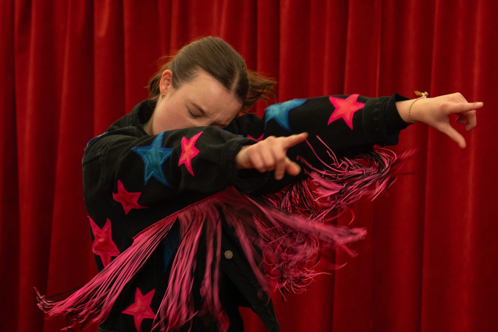 Bella Ramsey dancing in a jumper with stars and fringe