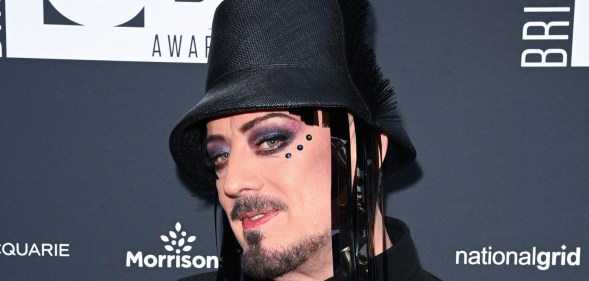 Boy George attends the British LGBT Awards 2026. He's wearing a black hat with fringe, three gemstones under his eye and a pistripe shirt