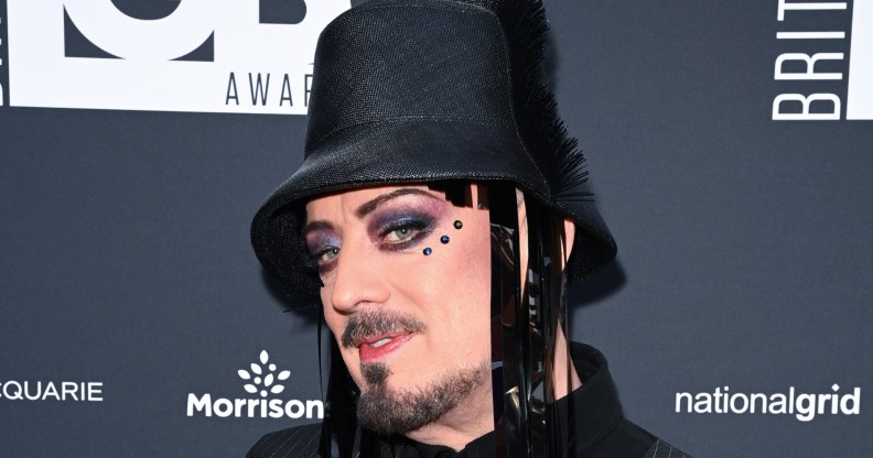 Boy George attends the British LGBT Awards 2026. He's wearing a black hat with fringe, three gemstones under his eye and a pistripe shirt