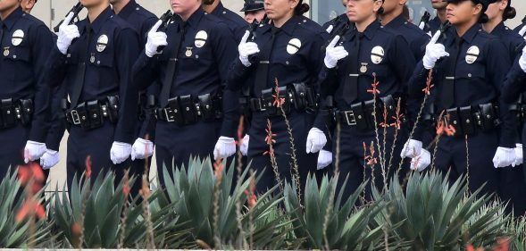 With black ribbons across their badge and holding a gun, police recruits attend their graduation ceremony at LAPD Headquarters