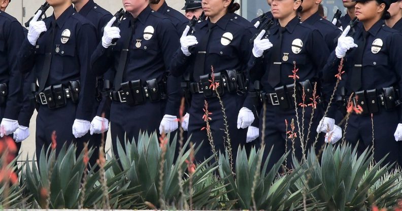With black ribbons across their badge and holding a gun, police recruits attend their graduation ceremony at LAPD Headquarters