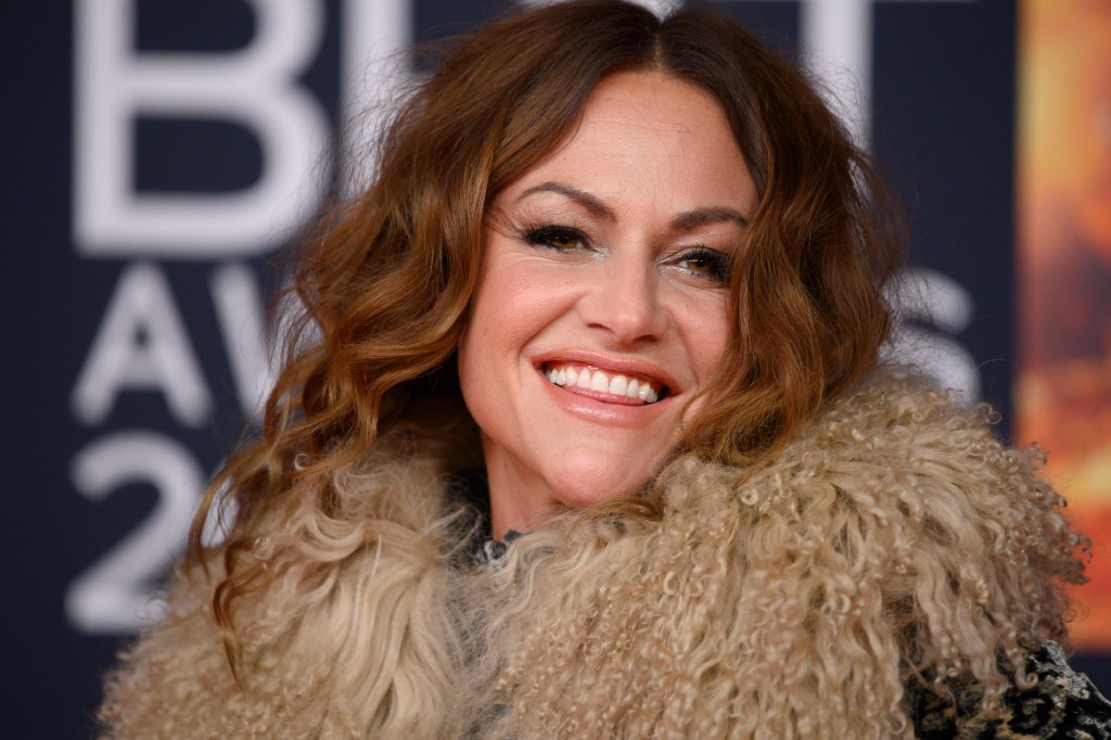 Jaime Winstone smiling at the camera in a fluffy collared coat