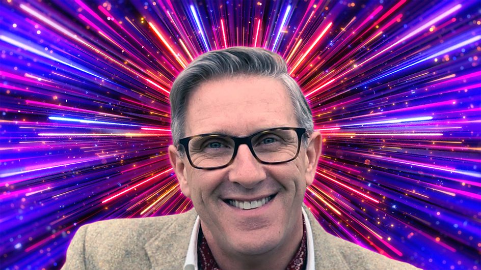 Graeme Hall in a cream suit with Strictly colourful fireworks behind him