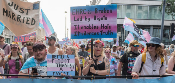 Trans people and allies at Trans+ Pride in London, with one person holding a sign criticising the EHRC.
