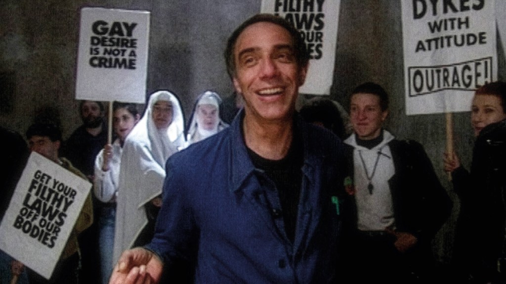 Queer Edward II: still of a smiling man amongst protesters