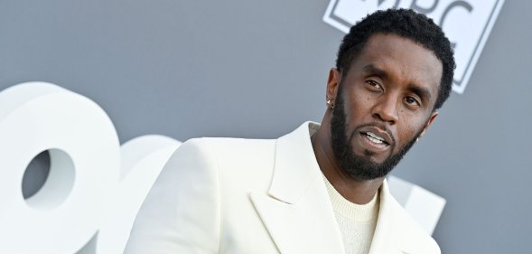 Music mogul Sean "Diddy" Combs wears a white shirt and matching suit while posing for a picture at an event
