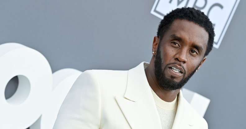 Music mogul Sean "Diddy" Combs wears a white shirt and matching suit while posing for a picture at an event
