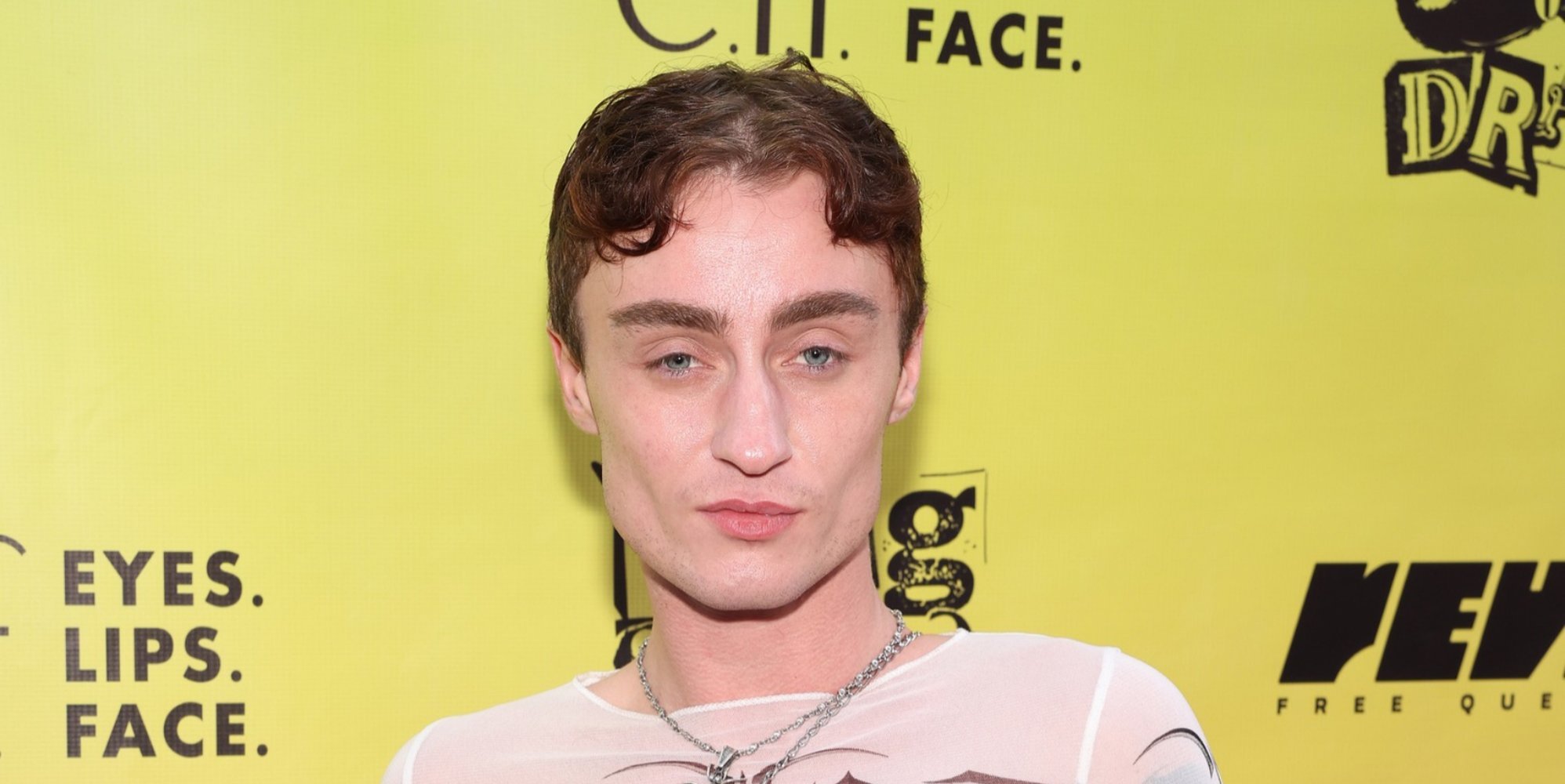 Drag performer Gottmik stands in front of a yellow background at an event.