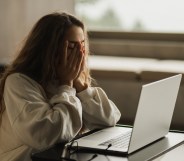 Woman covering her face in sadness, laptop in front of her