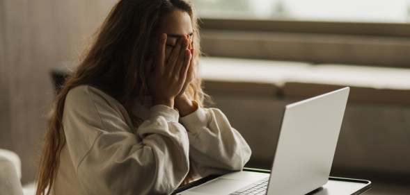 Woman covering her face in sadness, laptop in front of her