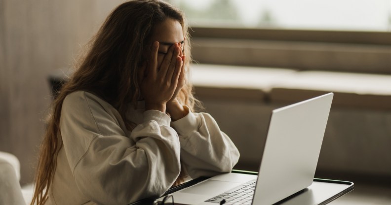 Woman covering her face in sadness, laptop in front of her